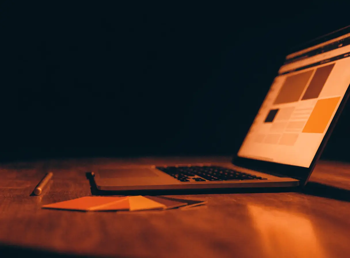 Laptop z projektem strony na ekranie, obok próbki kolorów i rysik